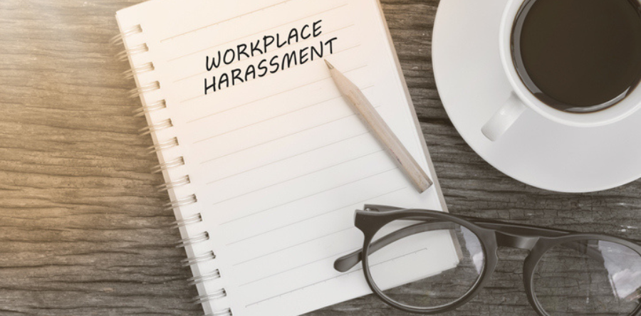 Workplace harassment written on notebook with glasses, pencil and coffee cup on wooden table